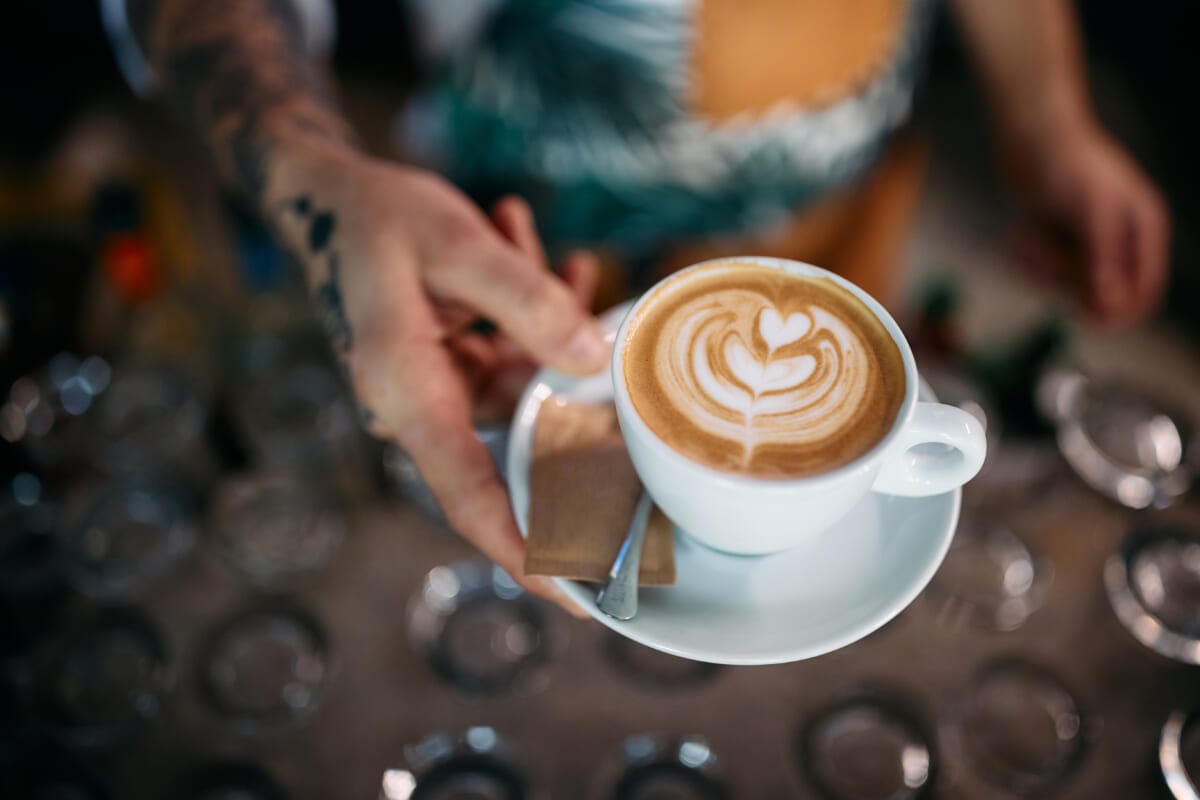 Closeup of waiter serving coffee with heart shape latte art on top | コーヒーステーション