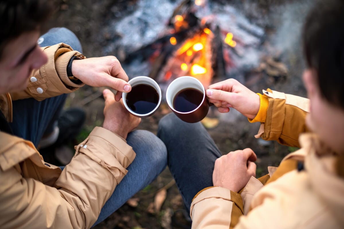 Two men clincking with cups of coffee on a picnic | コーヒーステーション