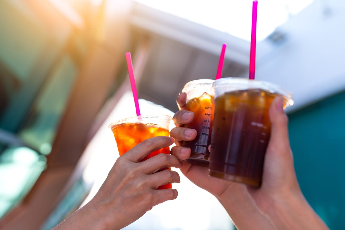 Friends holding iced coffee with sun flare | コーヒーステーション