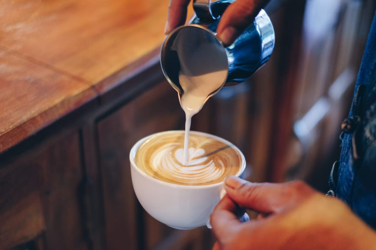 Hand barista pouring milk on coffee latte flower shape in cup | コーヒーステーション
