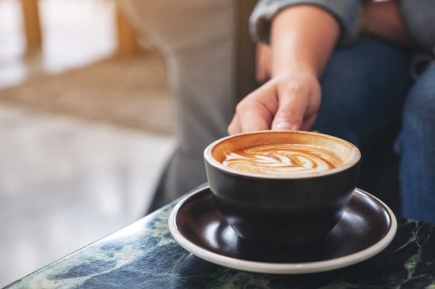 Closeup image of a hand holding a cup of hot coffee on table | コーヒーステーション