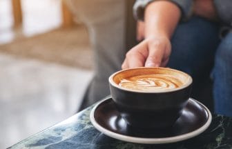 Closeup image of a hand holding a cup of hot coffee on table | コーヒーステーション