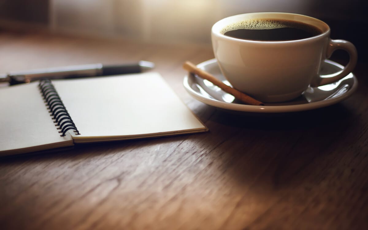 Closeup black coffee in cup with open blank notebook on wooden t | コーヒーステーション