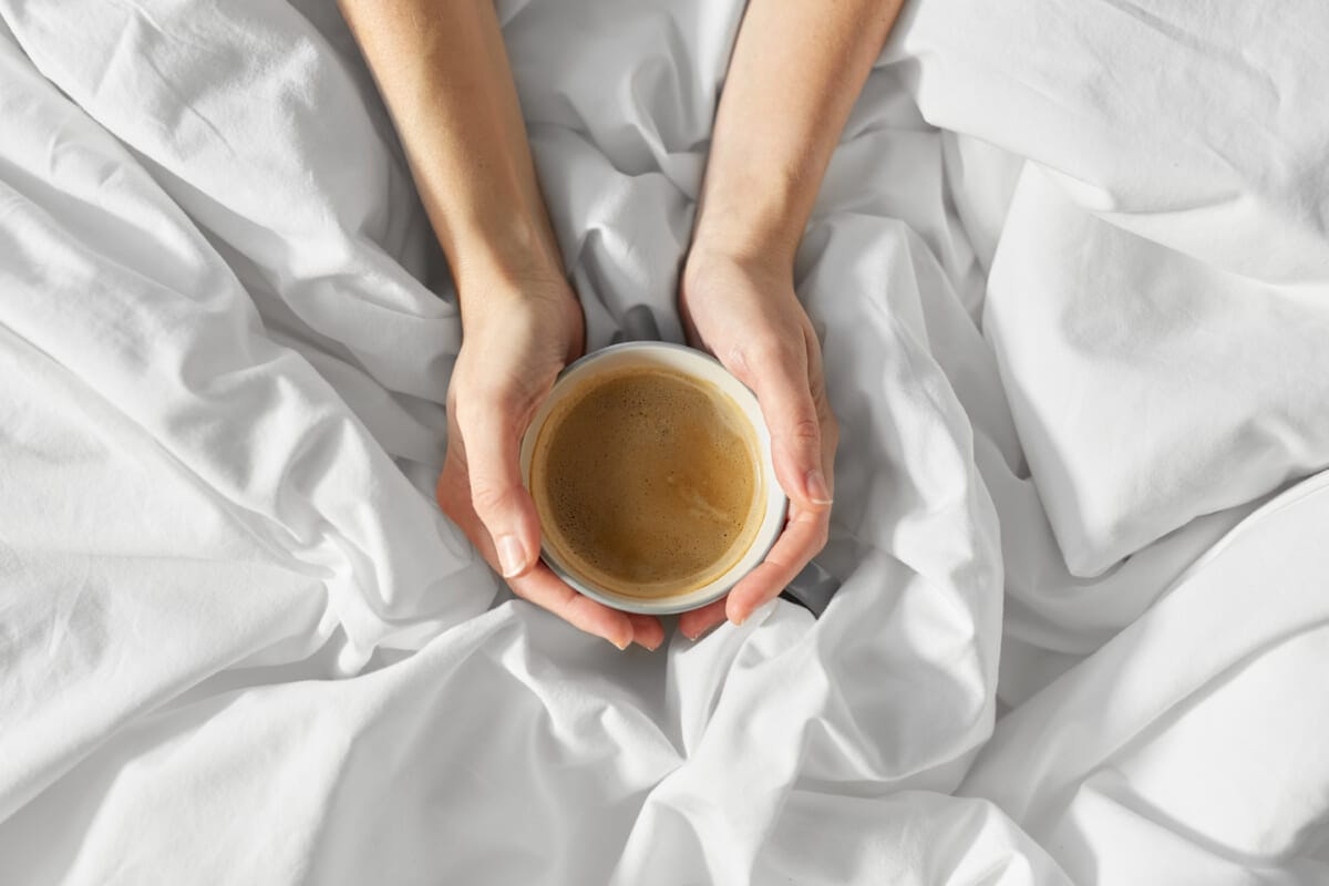 hands of woman with cup of coffee in bed | コーヒーステーション