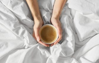 hands of woman with cup of coffee in bed | コーヒーステーション