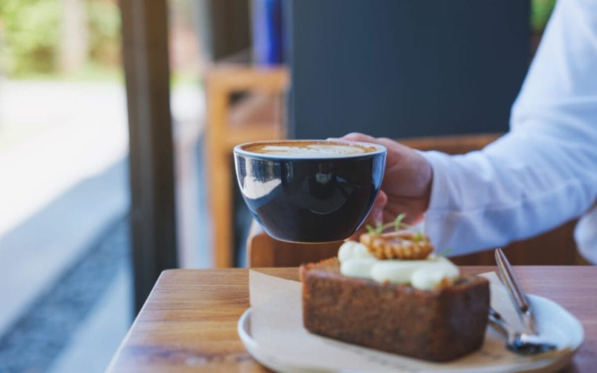 Closeup image of a woman holding and drinking coffee with a piece of carrot cake on the table | コーヒーステーション