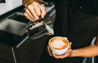 Crop image of a young male barista pouring hot milk into hot esp | コーヒーステーション