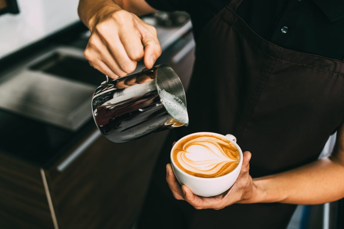 Crop image of a young male barista pouring hot milk into hot esp | コーヒーステーション