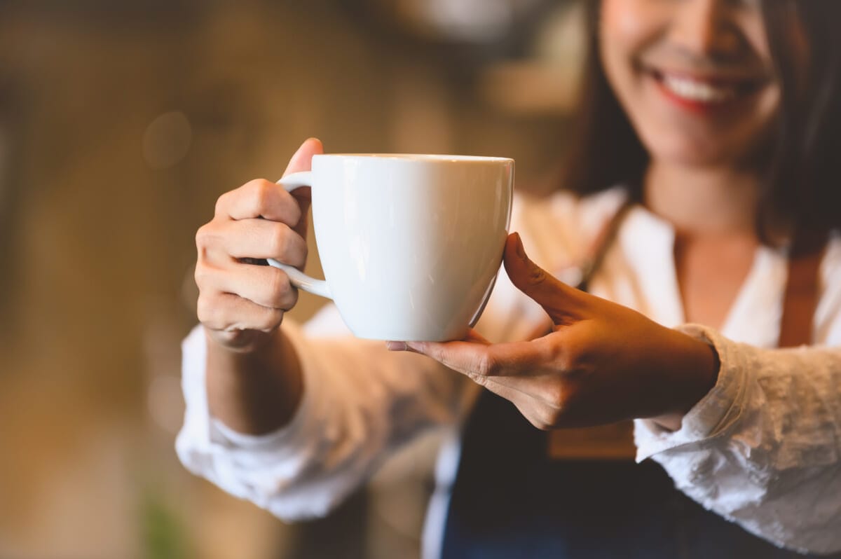 Closeup of white coffee cup with beautiful Asian woman barista b | コーヒーステーション