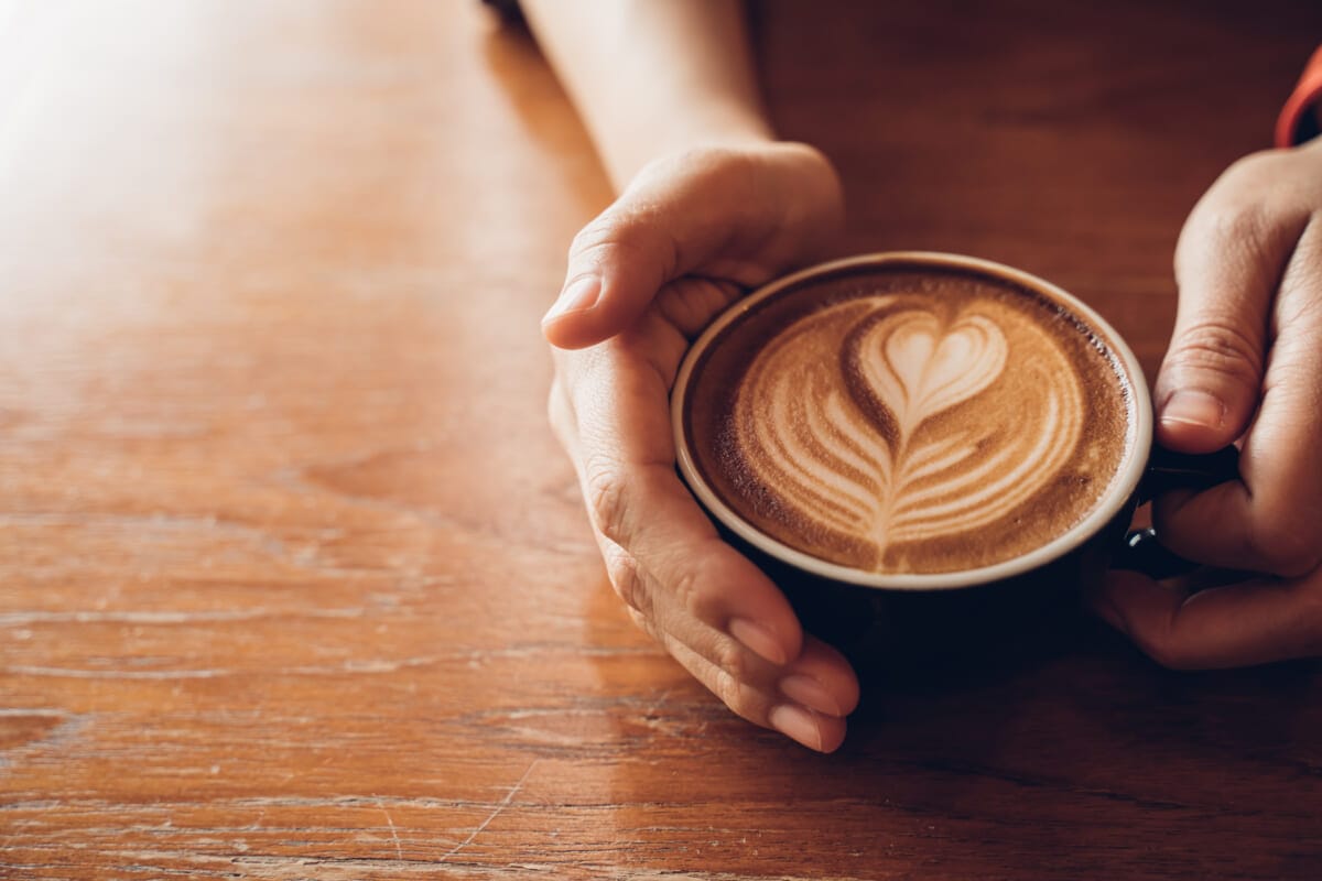 Close up Cup of coffee latte in coffee shopFemale hands holding | コーヒーステーション