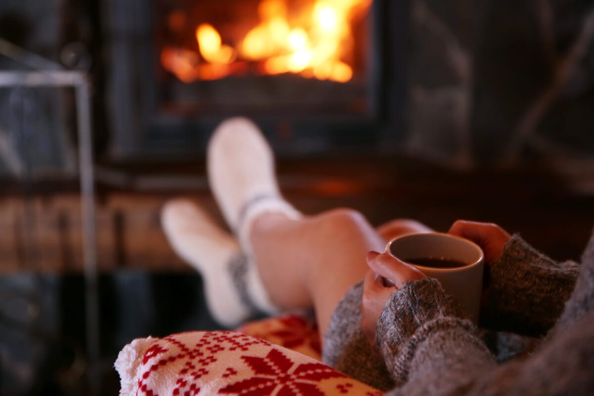 Woman resting with cup of hot drink near fireplace | コーヒーステーション