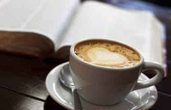 A cup of latte coffee on a tabletop next to a christian bible in spanish | コーヒーステーション