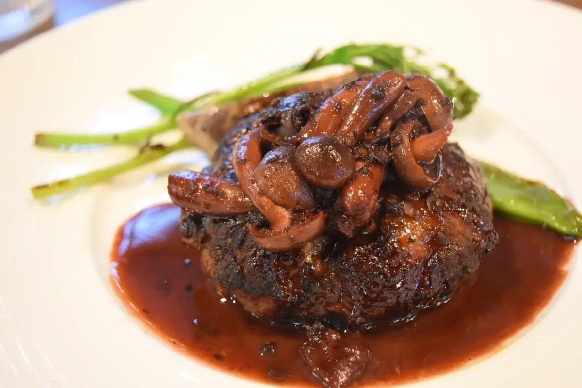 白い皿に盛られた、きのこがたっぷり乗ったハンバーグステーキ