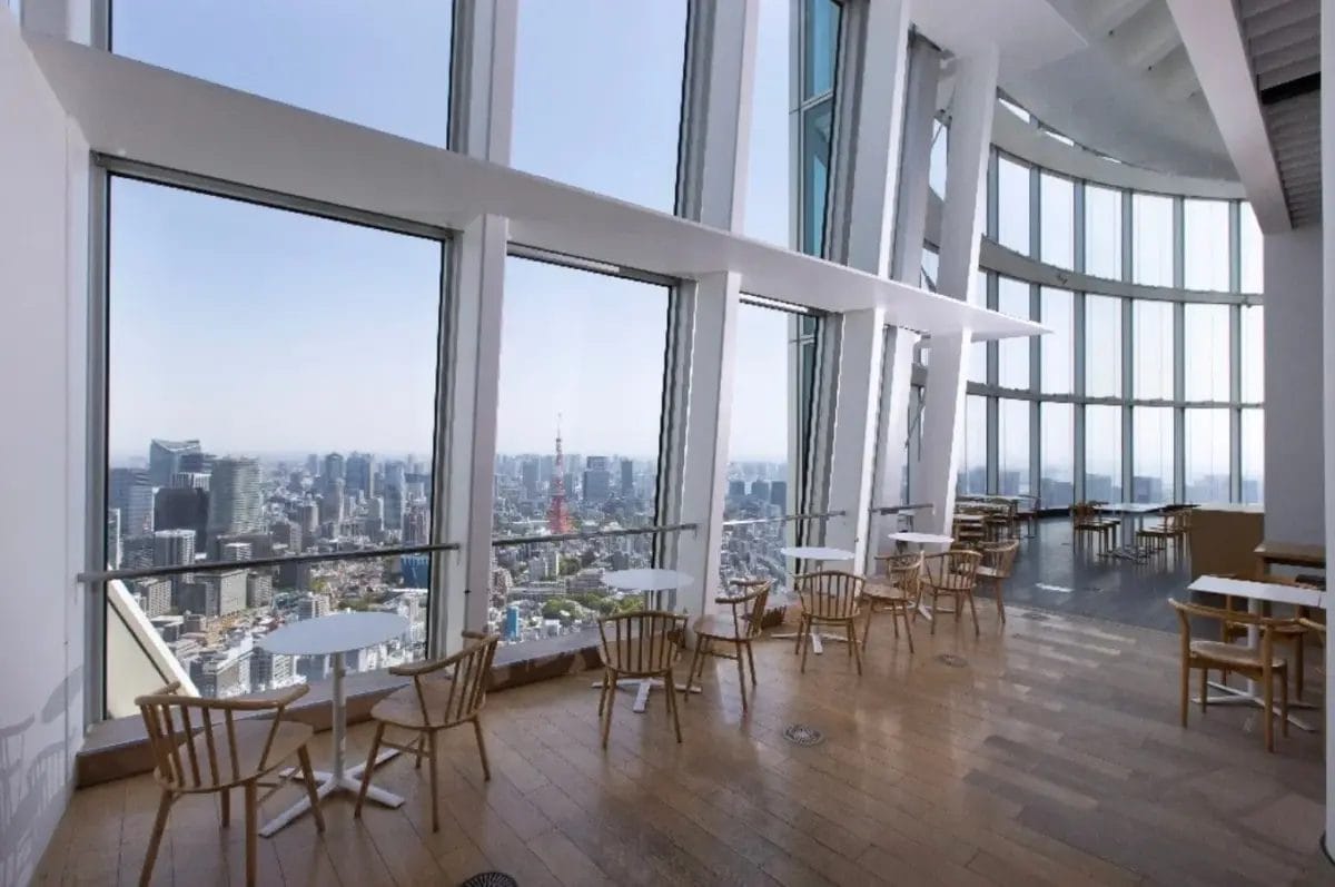 広々とした展望台のカフェまたはラウンジから、東京タワーを含む壮大な都市のパノラマ